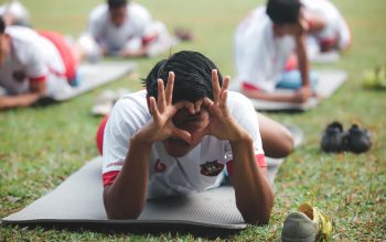 Atlet muda melakukan peregangan di atas matras di taman Jakarta selama latihan tim.