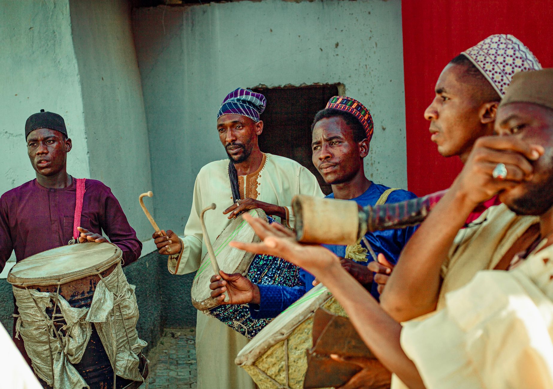 Sekelompok musisi Afrika memainkan instrumen tradisional di luar ruangan dengan pakaian yang cerah.